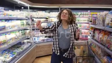 在<strong>超市</strong>：快乐的年轻女孩在<strong>超市</strong>的货架之间滑稽地跳舞。 穿牛仔裤和黑色的卷发女孩